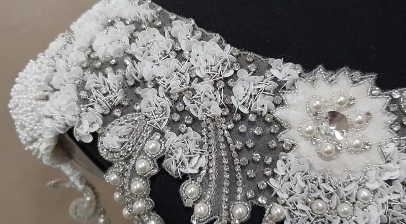 White floral beadwork, pearl-like beads, sequins and reflective embellishments on dark fabric.