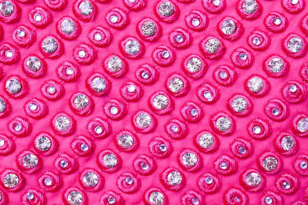 Reflective round embellishments arranged in rows on bright pink fabric.