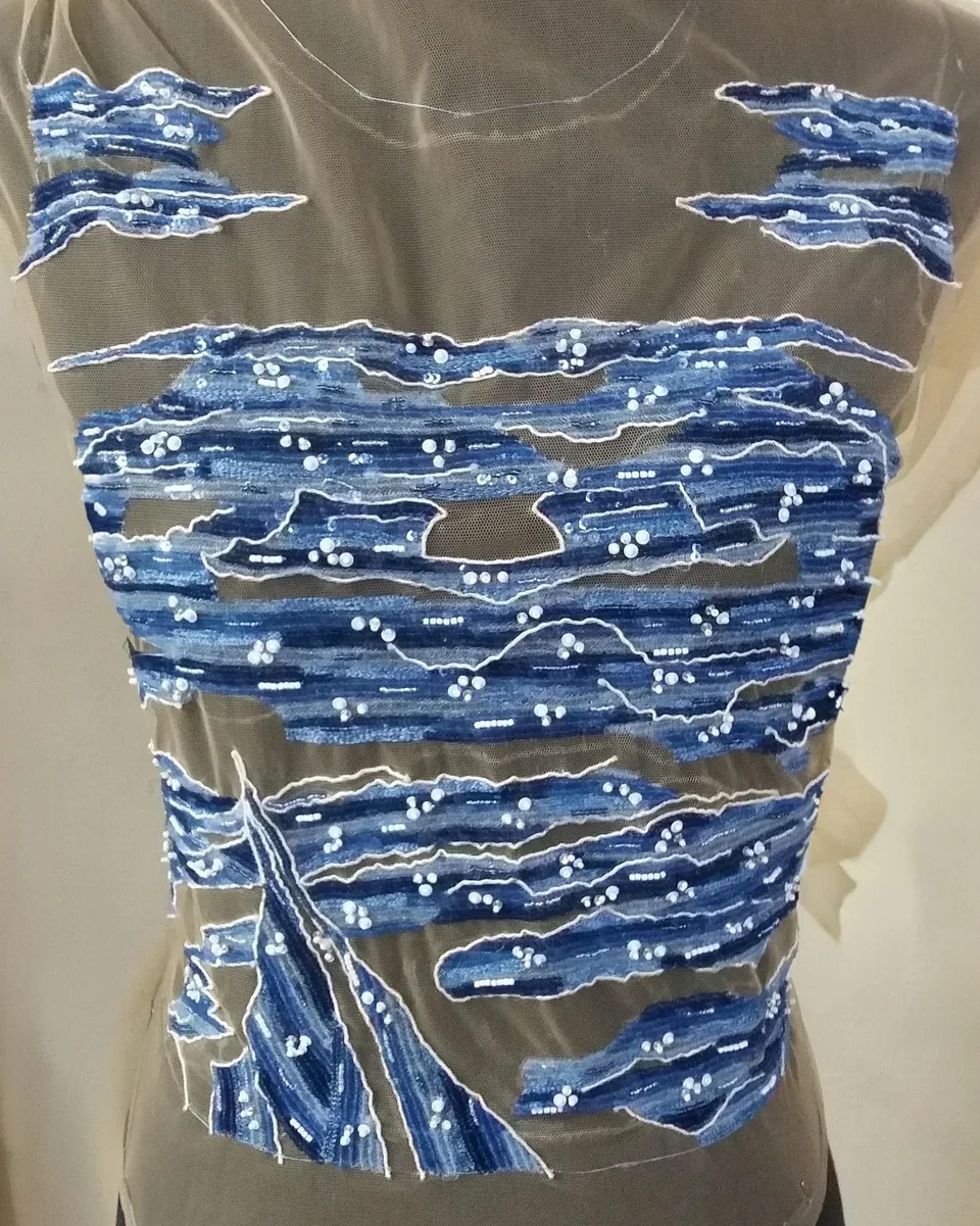 Blue wave-like embroidered bands with pale dots across a transparent top on a dress form.