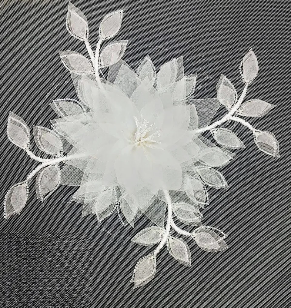 Large layered white flower surrounded by delicate leaves on transparent net.