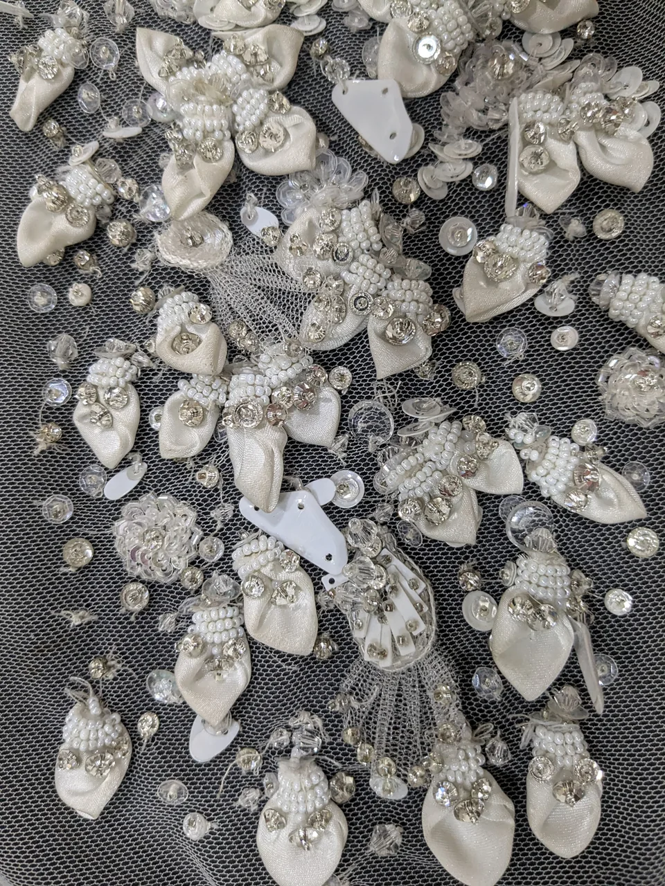 Dense pale embellishment with folded petal shapes and scattered reflective accents on open net.