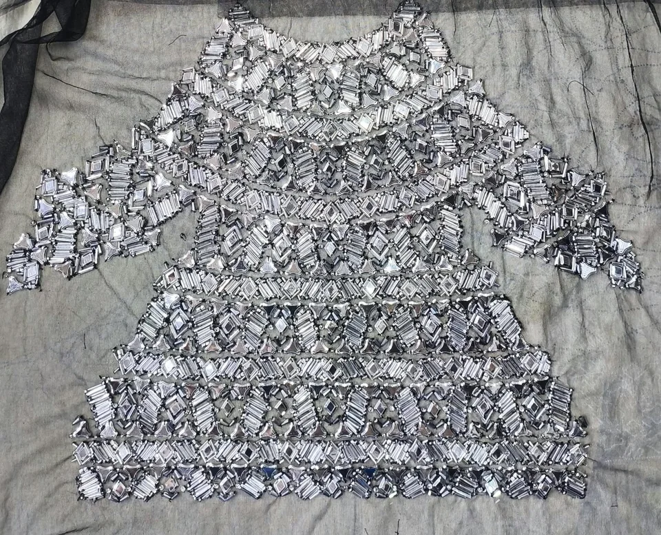 Complete bodice-shaped arrangement of reflective geometric motifs laid flat on dark net.