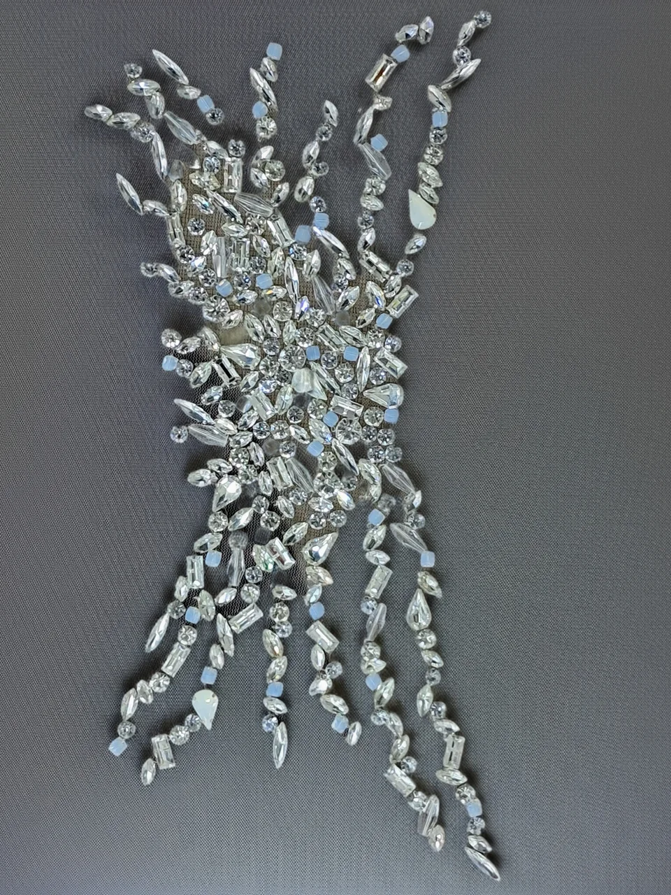 Radiating arrangement of clear-looking faceted and rounded embellishments on grey net.