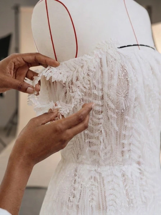 Hands inspecting the embellishment of an ivory garment on a dress form